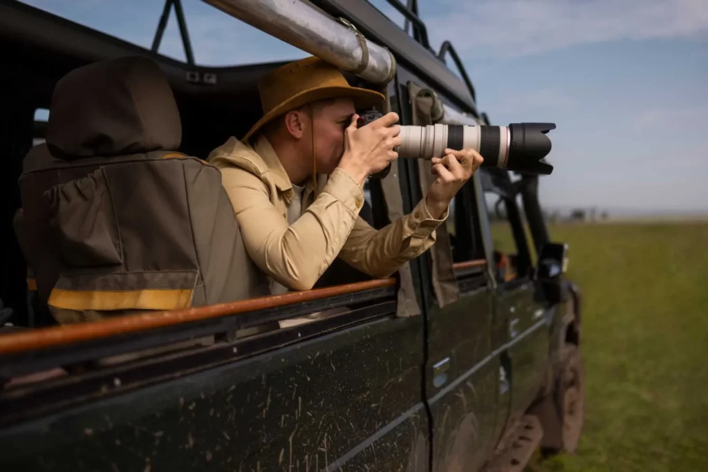 A photographer in a safari game drive vehicle points a camera with a long lens out of the vehicle