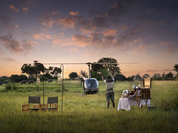 A staff member welcomes back guests on a private helicopter tour with sundowner drinks in the bush in Botswana