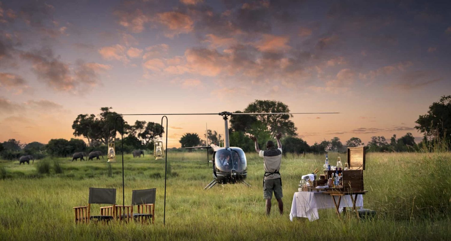 A staff member welcomes back guests on a private helicopter tour with sundowner drinks in the bush in Botswana
