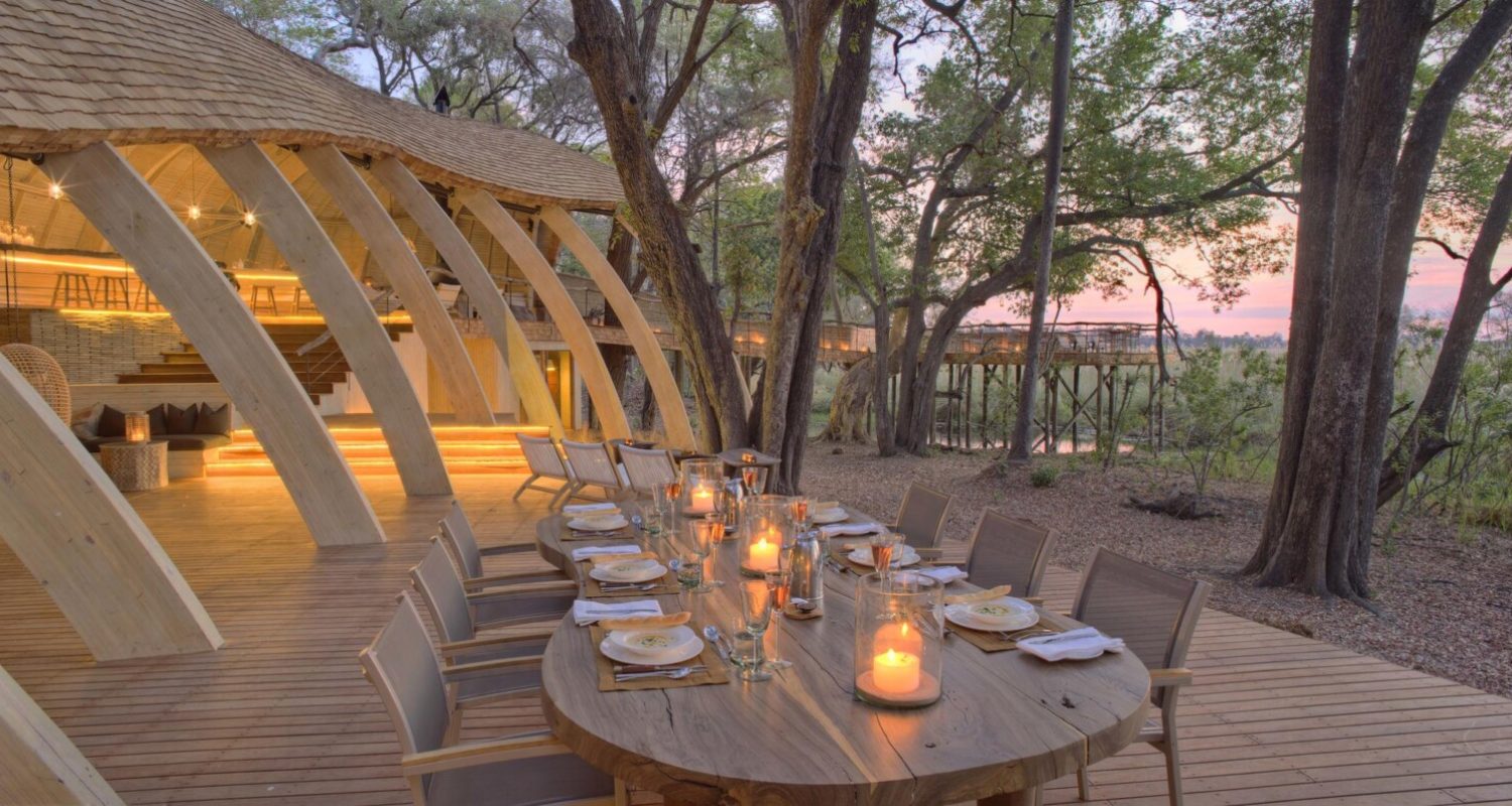 An elegantly designed long outdoor dining table with a modern-rustic feel and candles at Sandibe Okavango Safari Lodge