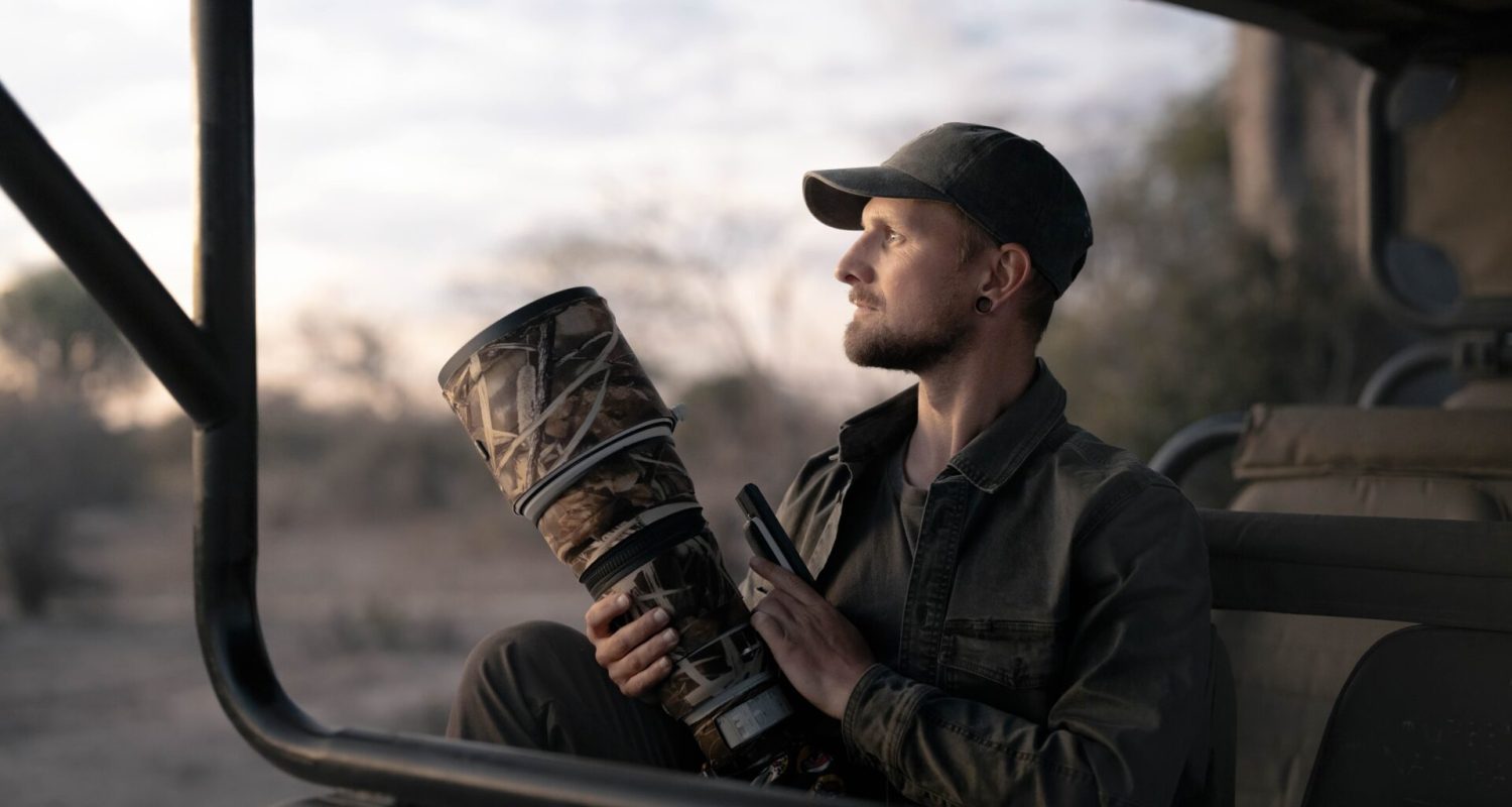 Photographic guide and workshop host Andrew Macdonald sits in wait in a safari vehicle, holding a long lens camera